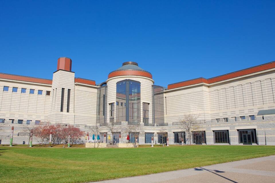 A large, modern building with a central dome and two towers, surrounded by a well-maintained lawn and a clear blue sky.