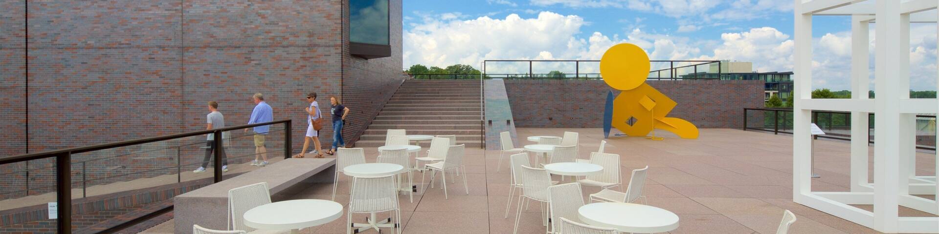 A modern building with a brick facade, outdoor seating area, and a large yellow sculpture.