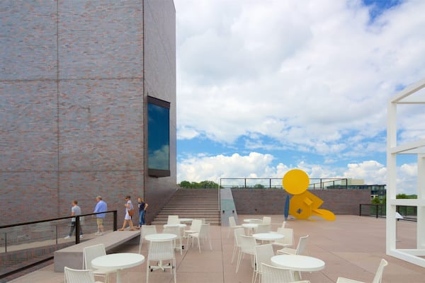 Un bâtiment moderne avec une façade en briques, un espace extérieur aménagé pour s’asseoir et une grande sculpture jaune.
