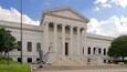 A neoclassical building with a grand entrance, large columns, and a statue.