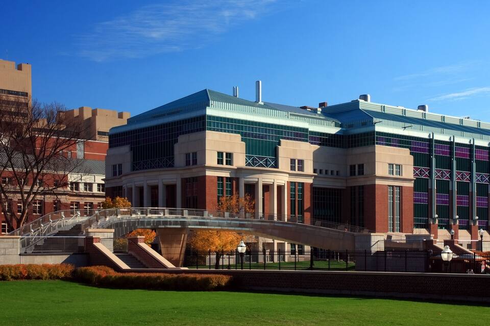 A modern building with a glass facade, a bridge, and a well-maintained lawn.