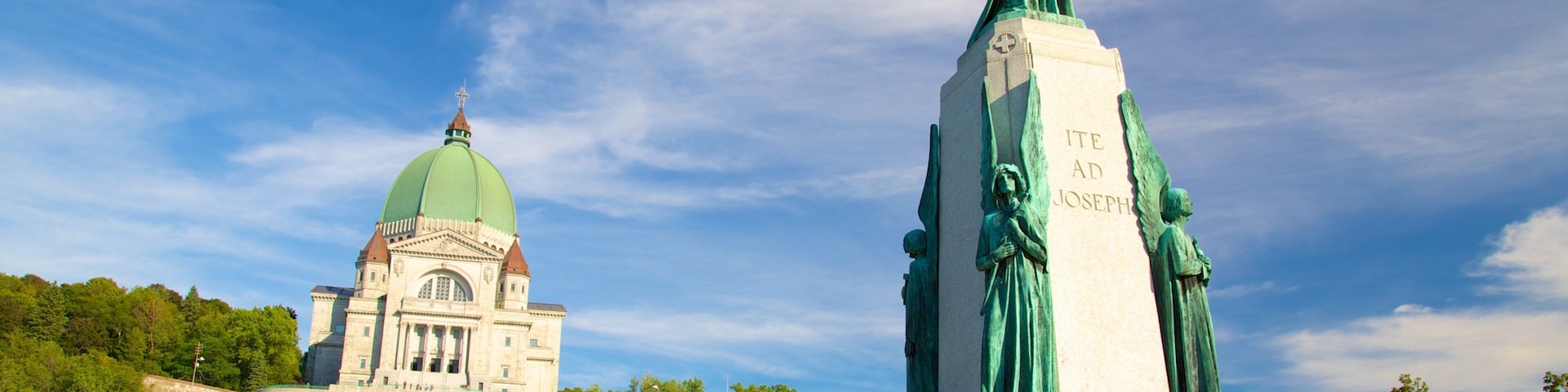 A statue of a religious figure with inscriptions, a large green-domed building, and a well-maintained park with pathways.