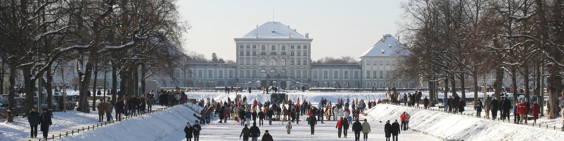 Nymphenburg Palace featuring a park and snow as well as a large group of people