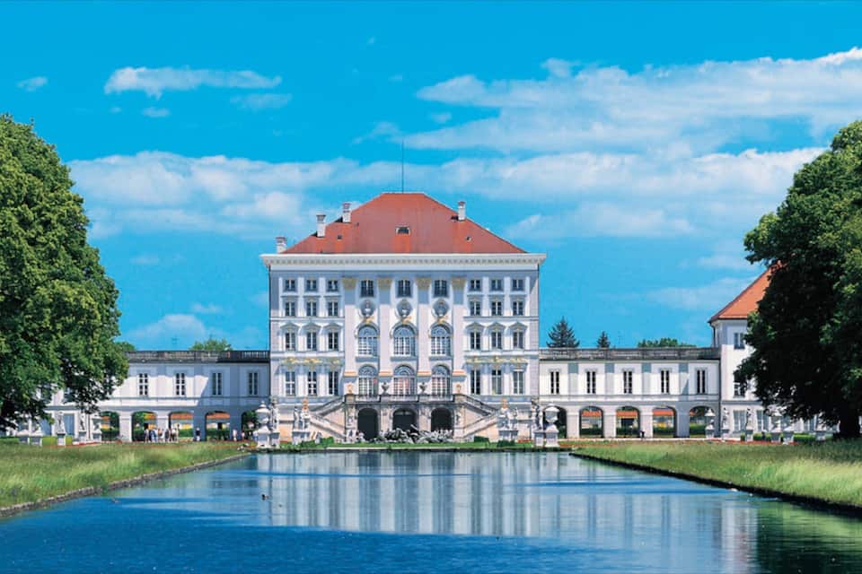 Ein großes, historisches Gebäude mit rotem Dach, umgeben von einem Kanal und Bäumen.