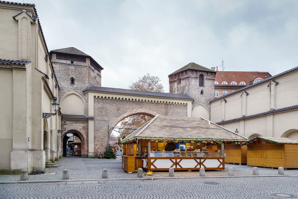 A cobblestone street with a market stall and a historic building with brick walls and arches.