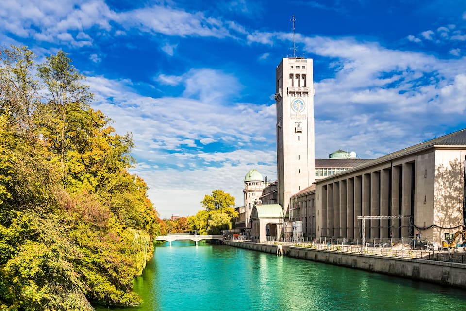 A river with a bridge, a clock tower, and a large building with columns.