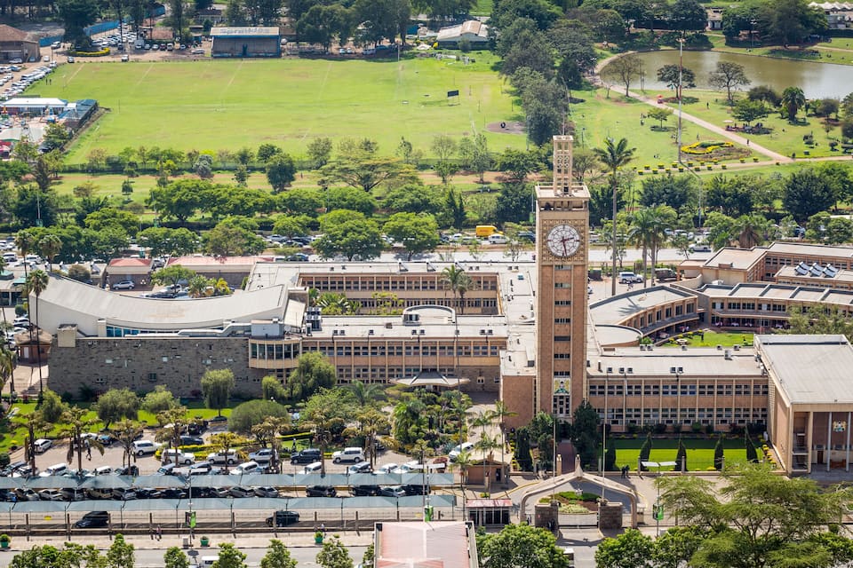 A large building with a clock tower, surrounded by green spaces and a parking lot.