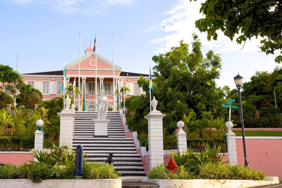 Um edifício rosa com uma estátua, rodeado por vegetação e um hidrante vermelho.