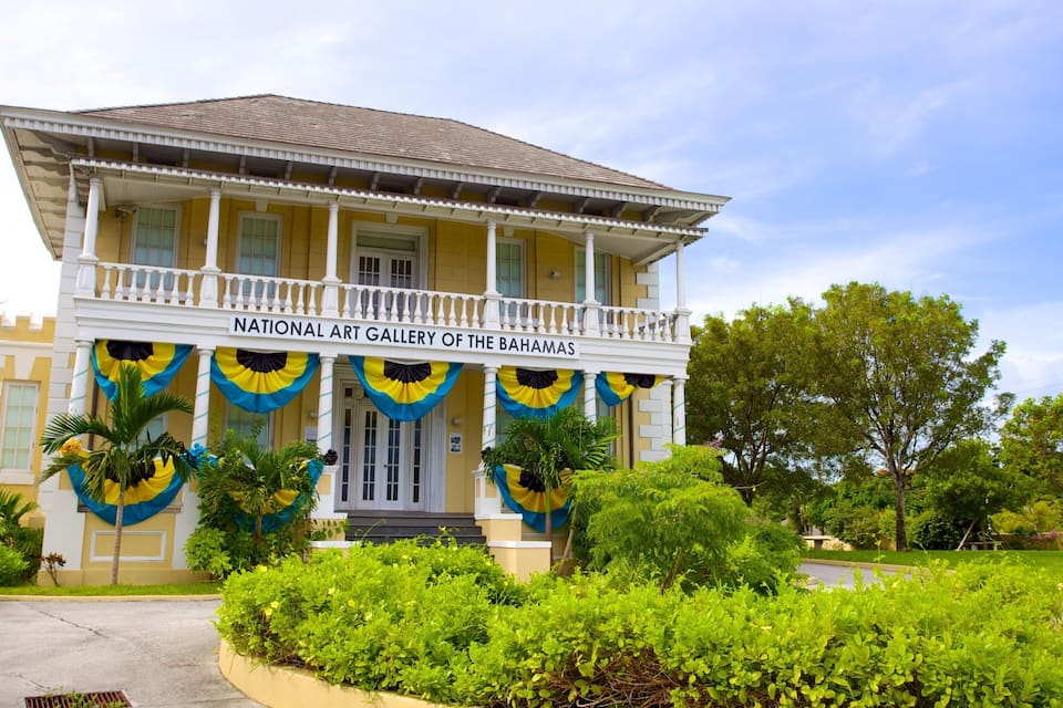 Um edifício amarelo com varanda e uma placa que diz 'National Art Gallery of the Bahamas'.