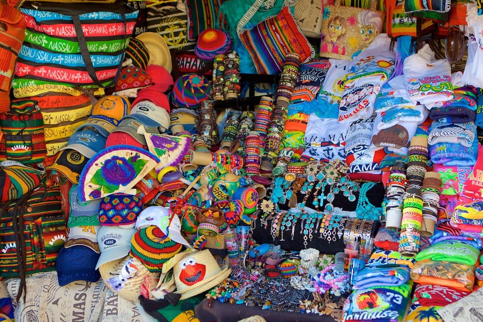 Diversos artigos de recordação e artesanato coloridos, incluindo chapéus, bolsas e joias, com texto visível como "Bahamas" e "1973".