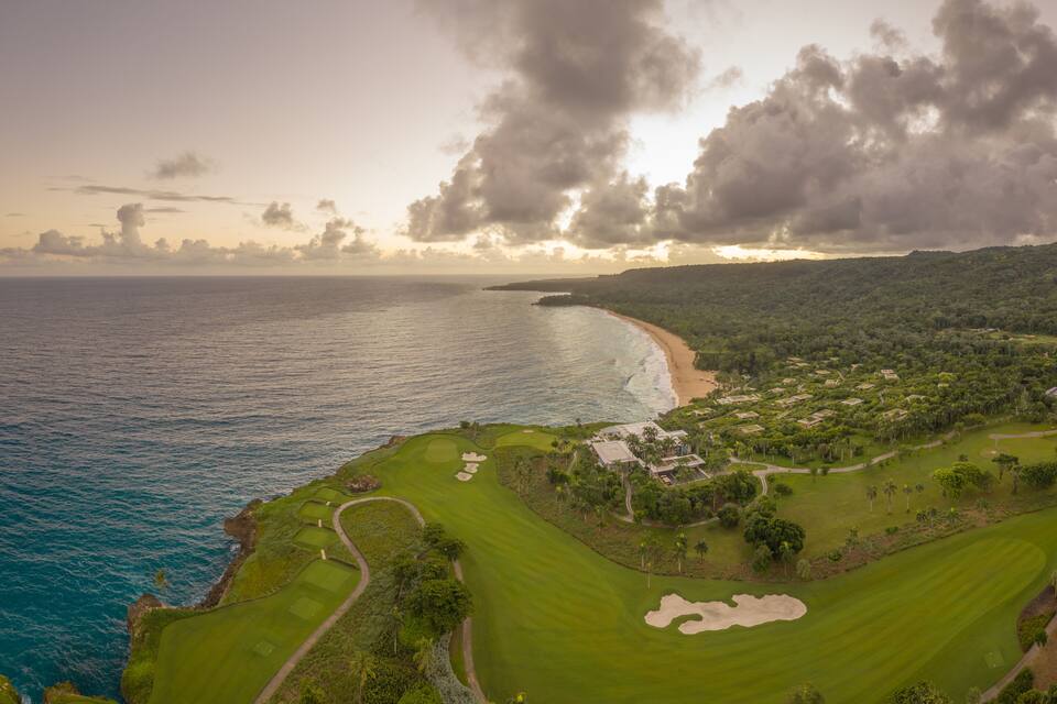 Ein Küsten-Golfplatz mit Strand, Meer und üppiger Vegetation.