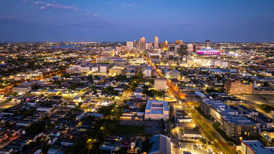 Aerial view of New Orleans skyline illuminating at dusk, showcasing vibrant city lights, prominent buildings, and the iconic Caesar Superdome under a beautiful twilight sky