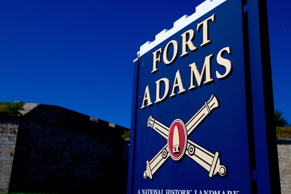 A sign for Fort Adams, a National Historic Landmark, with crossed cannons and a clear blue sky in the background.
