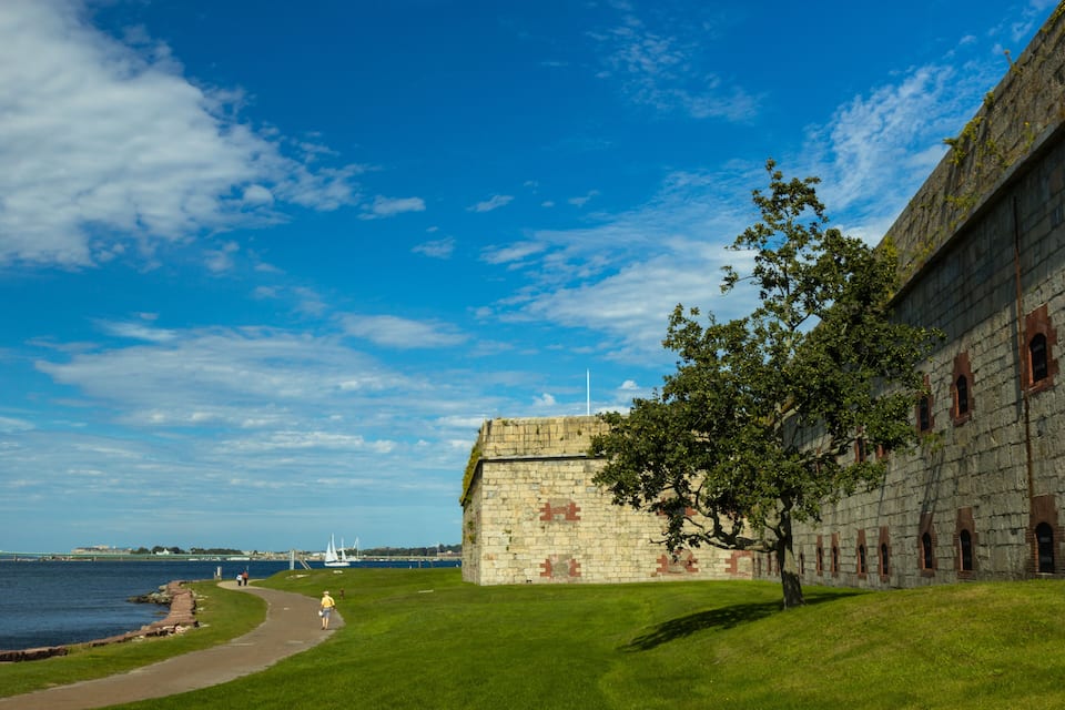 En byggnad av sten med en gräsyta och en stig som löper längs med en vattenyta.