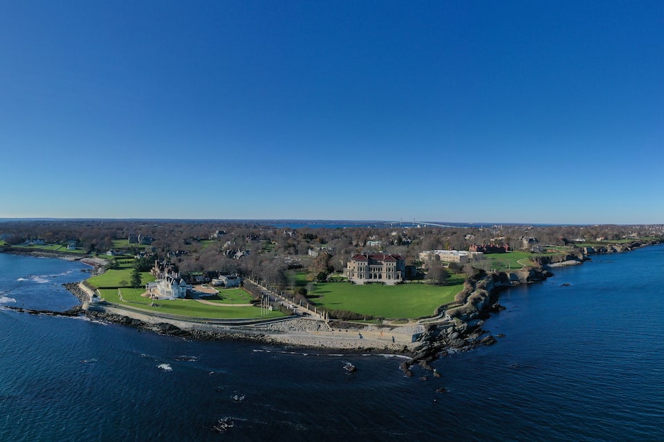 An aerial view of a coastal town with a prominent island featuring a large house, a golf course, and a rocky shoreline.