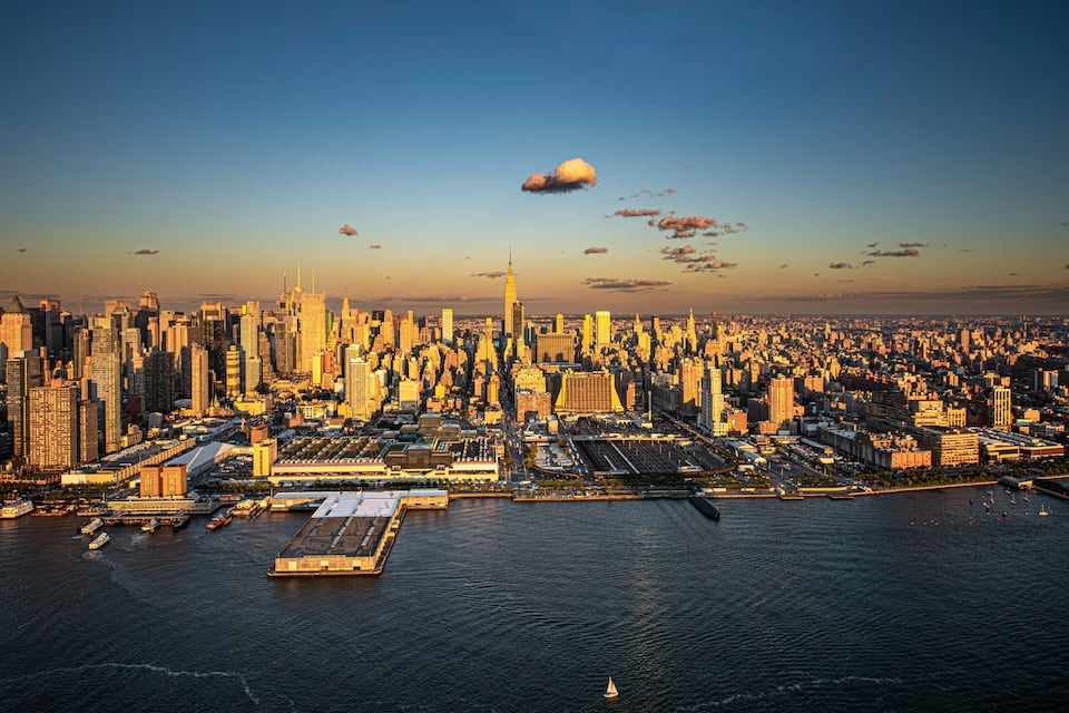 A city skyline with a prominent skyscraper, a large body of water, and a clear sky.