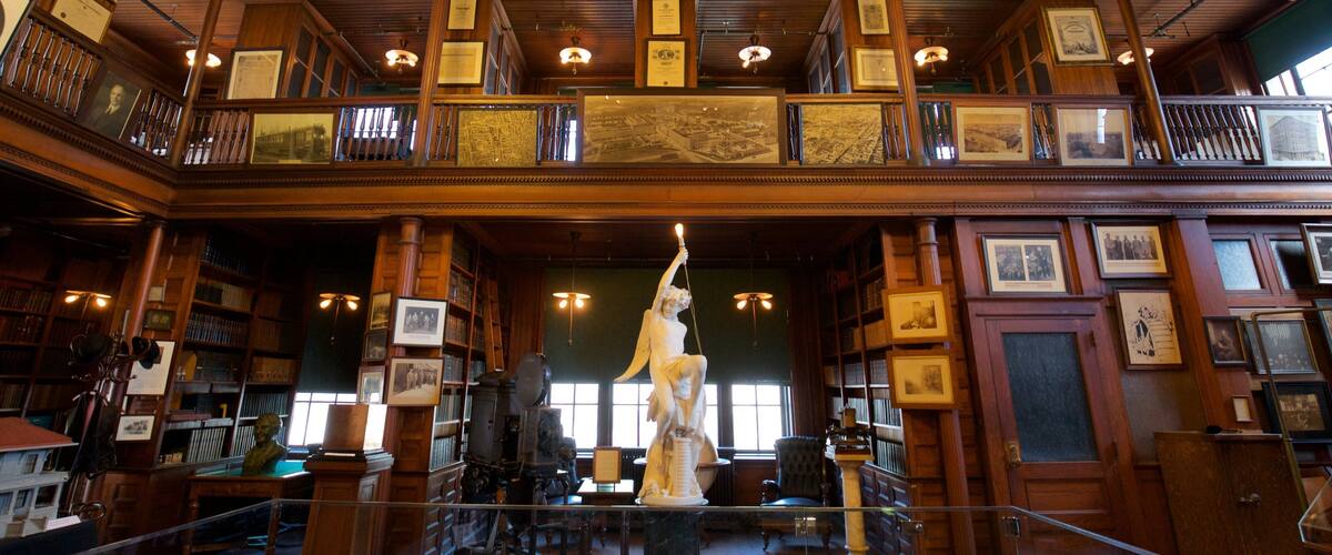 A grand library with wooden architecture, multiple levels, and a statue in the center.