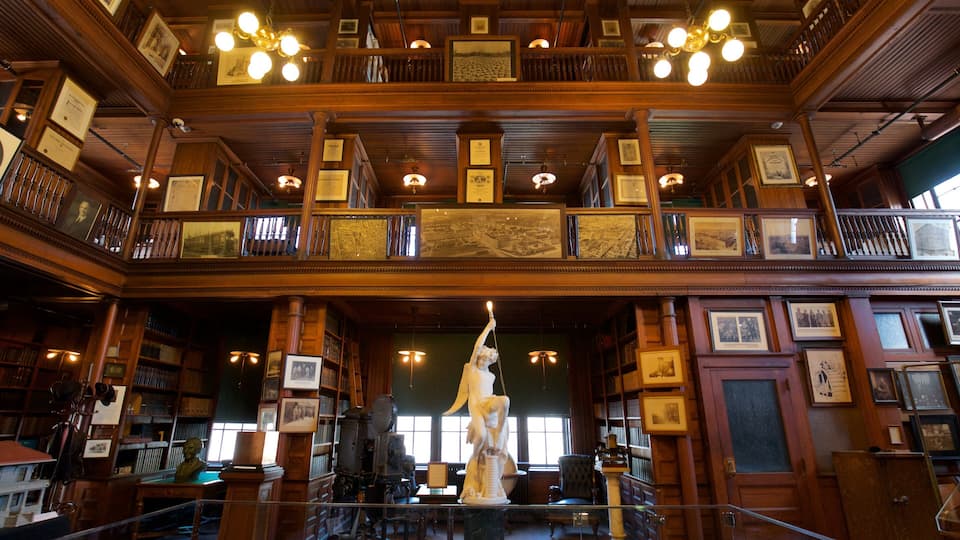 A grand library with wooden architecture, multiple levels, and a statue in the center.