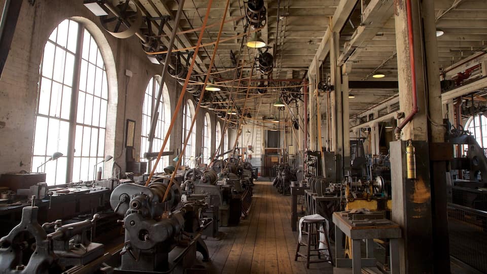 An industrial building with large windows, machinery, and wooden floors.