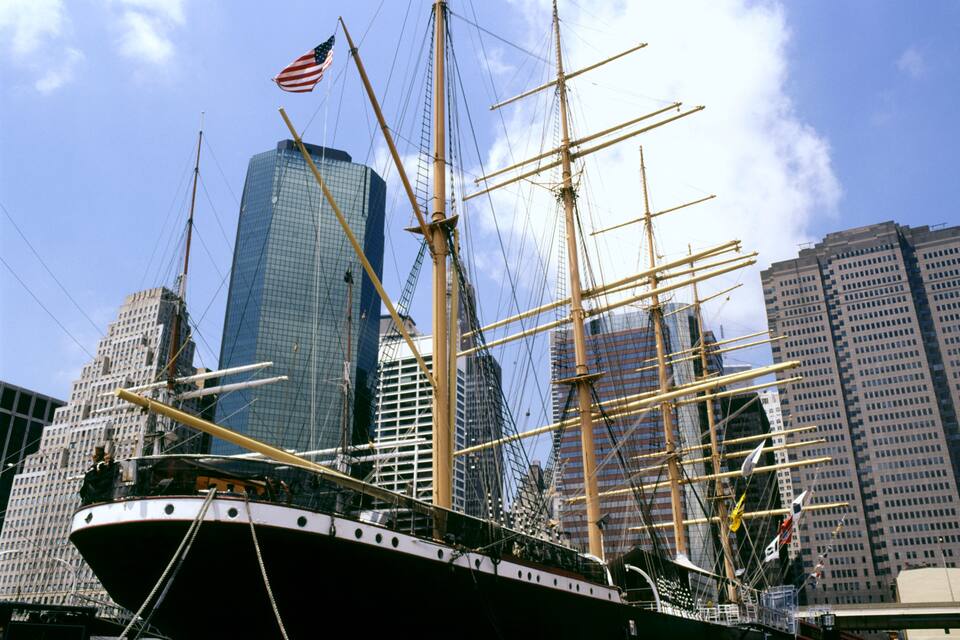 A tall ship with masts and rigging in a cityscape with modern skyscrapers.