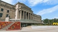 A large neoclassical building with columns and a statue, labeled 'Brooklyn Museum.'