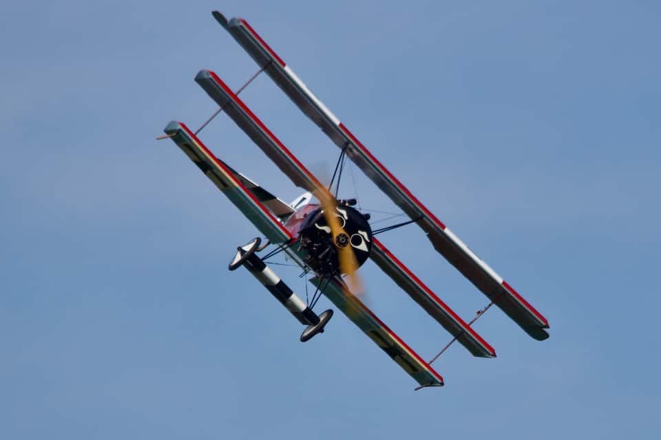 Un avion biplan aux rayures rouges et blanches volant dans un ciel bleu dégagé.