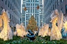 A Christmas tree, illuminated sculptures, and a statue in an urban setting.