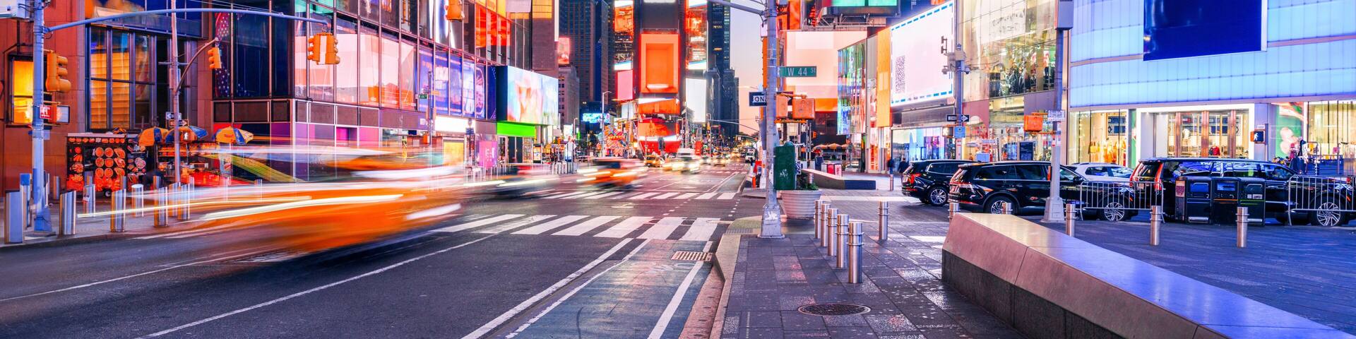 A city street at dusk with illuminated billboards and skyscrapers.