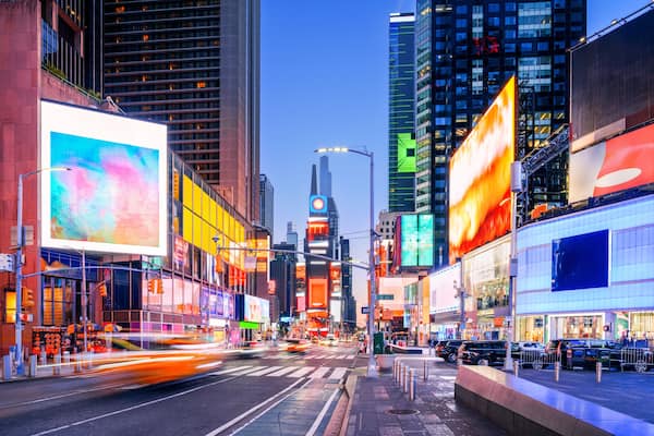 A city street at dusk with illuminated billboards and skyscrapers.