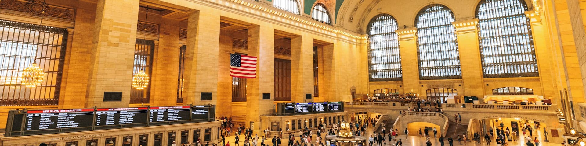 A spacious train station with high ceilings, large arched windows, and an American flag.