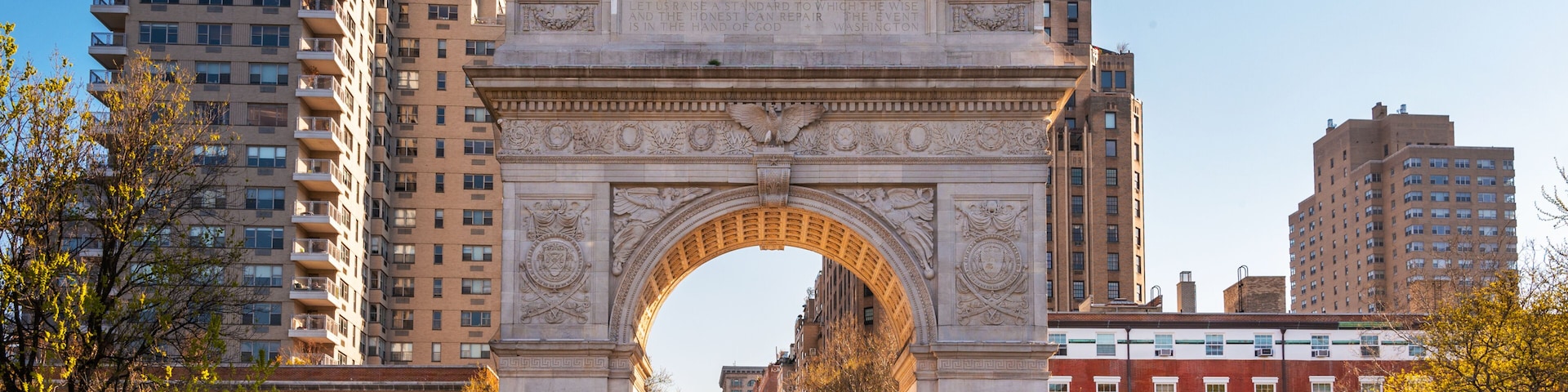 An ornate stone archway with intricate carvings, surrounded by modern high-rise buildings and a red brick building.