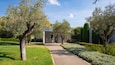 A pathway leading to a modern building with glass doors, surrounded by lush greenery and trees.