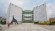 A modern building with a curved glass facade and a large sculpture in front.
