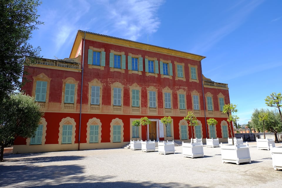 A red building with green shutters and white planters in front.
