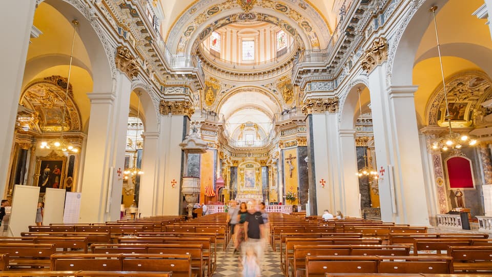 An ornate church interior with high ceilings, detailed frescoes, and rows of wooden pews.