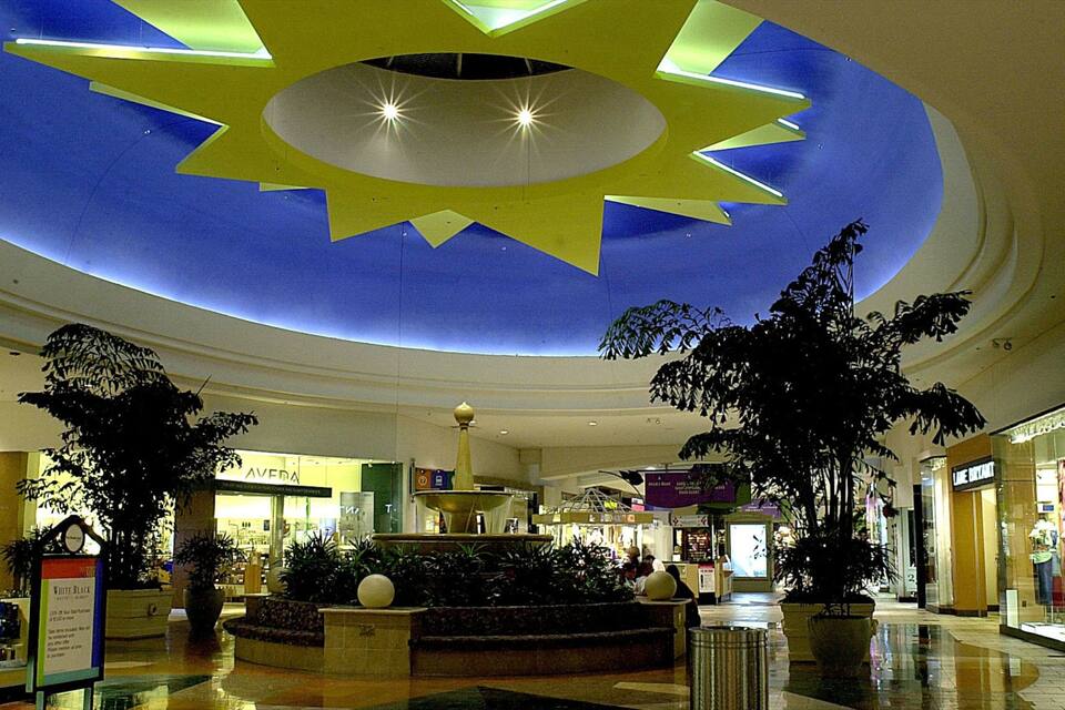 Um shopping center com um grande desenho de estrela iluminada no teto, plantas em vasos e diversas lojas, incluindo Aveda e Nike.