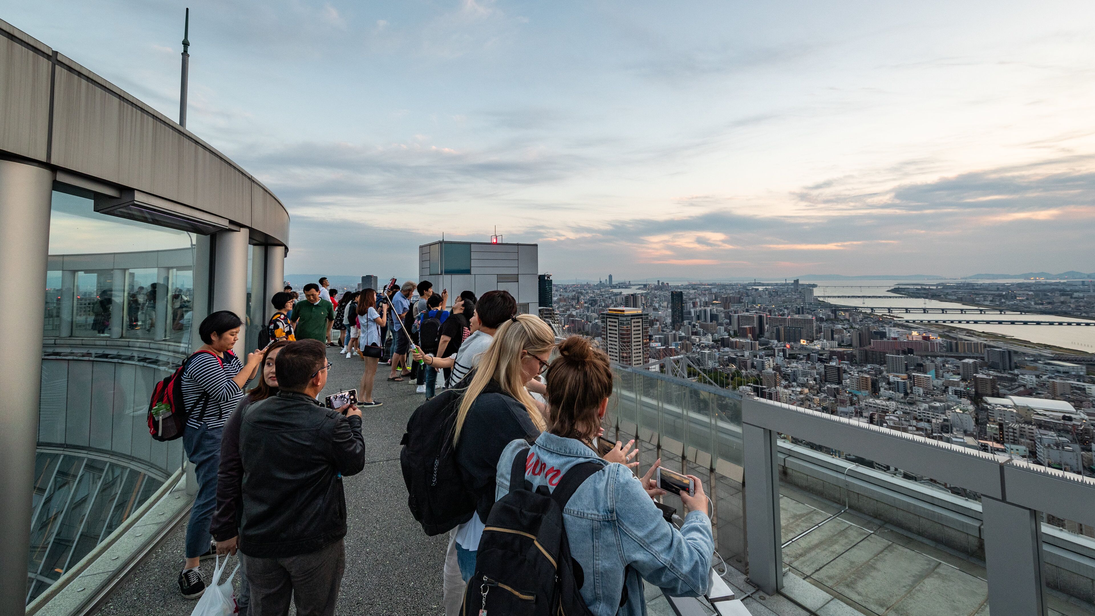 A group of people on a glass observation deck overlooking a cityscape with a river and bridges.