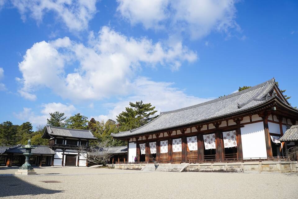 A traditional Japanese temple with a large courtyard, wooden buildings, and a clear blue sky.