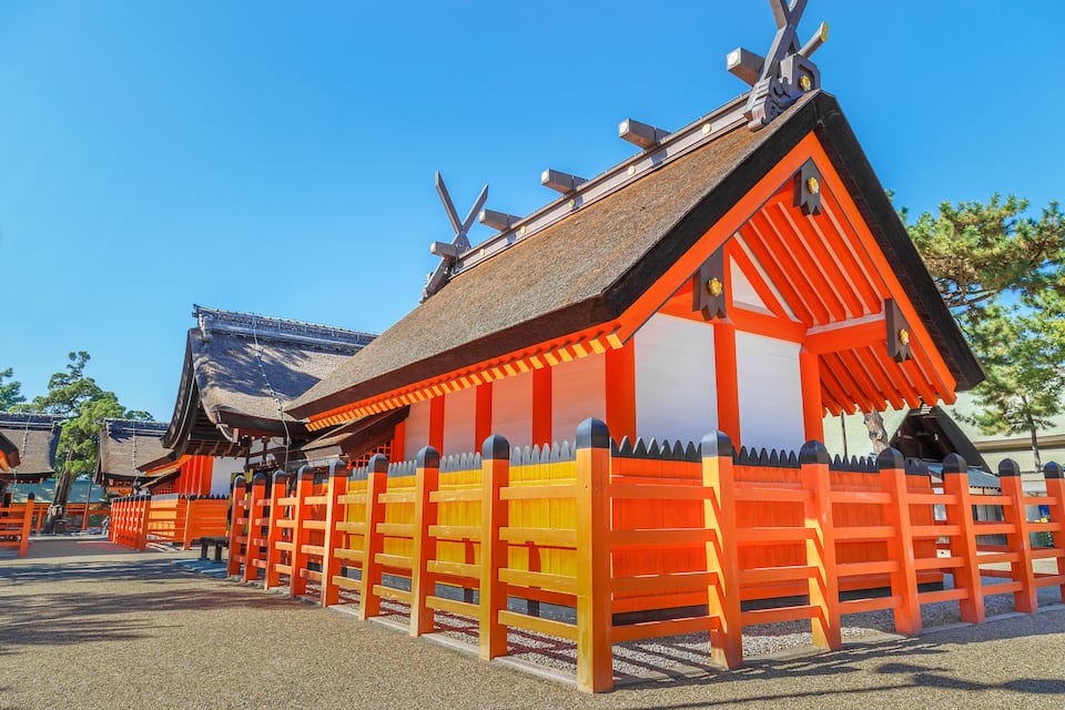 A traditional Japanese building with bright orange and white walls, a thatched roof, and a fence with a picket design.