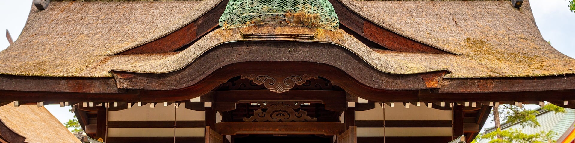 A traditional Japanese temple with a thatched roof, wooden beams, and a red entrance gate.