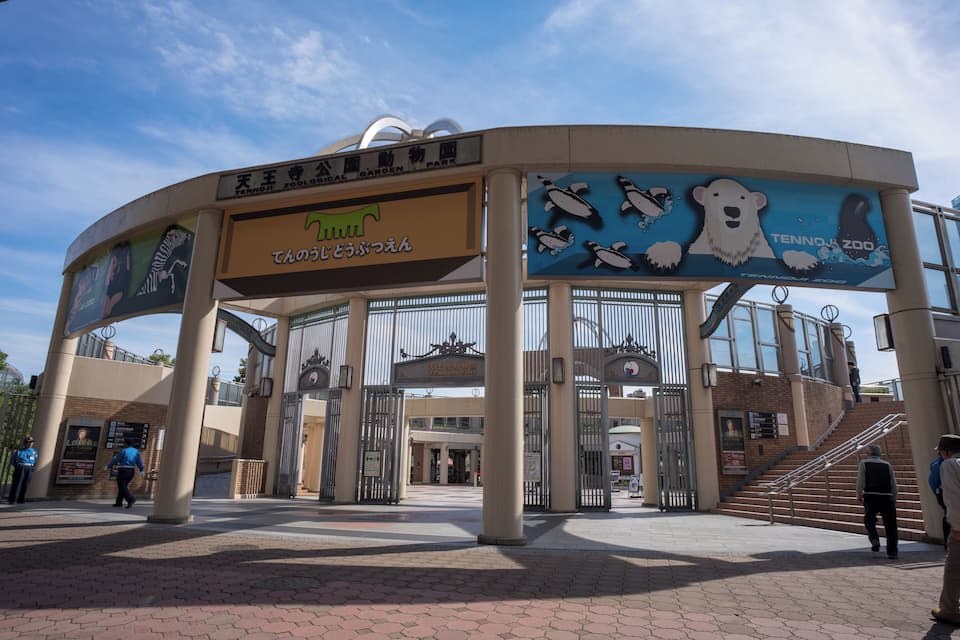 Entrada de um jardim zoológico, com uma placa indicando o Zoológico Tennozu e uma ilustração de um urso polar.
