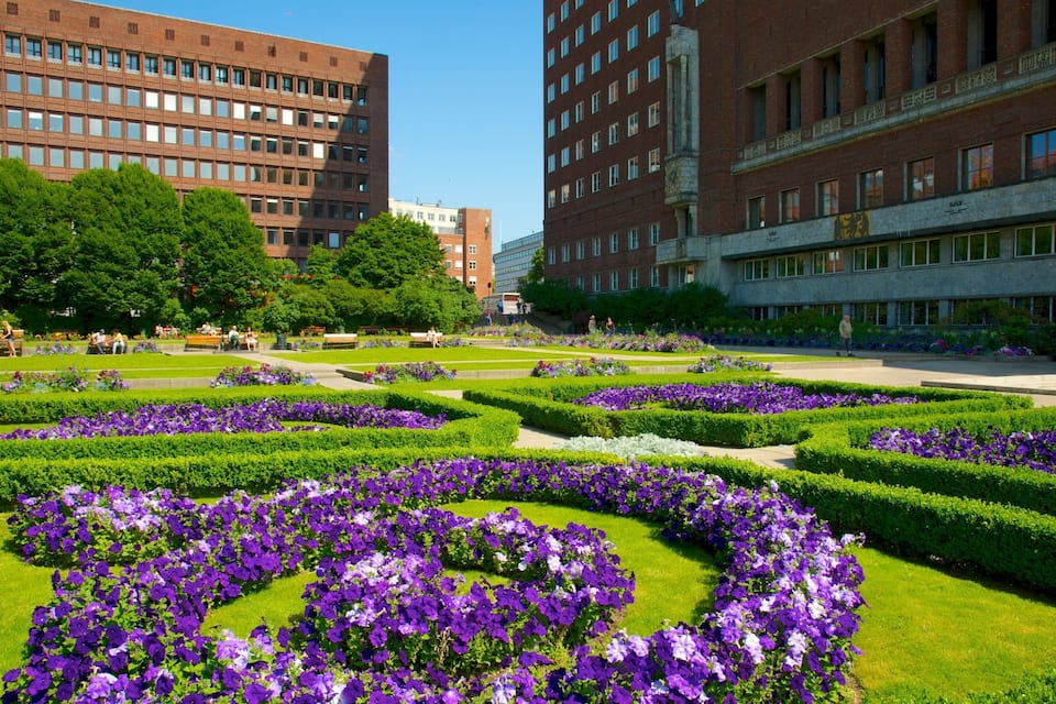 A park with manicured flower beds and modern buildings in the background.