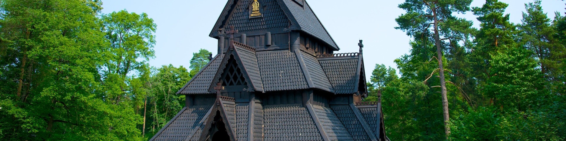 Um edifício de madeira escura com telhado íngreme, rodeado por árvores verdes exuberantes.