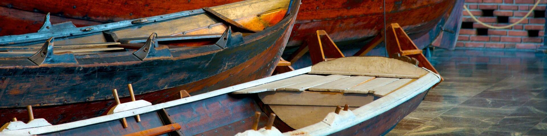 Several wooden boats with metal fittings, displayed against a brick wall.