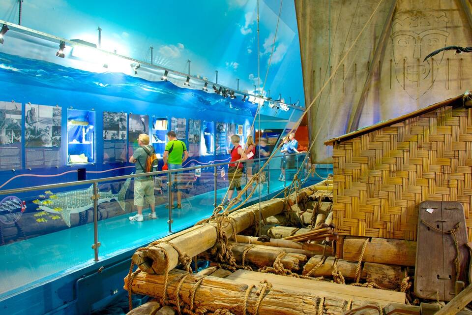 An indoor maritime exhibit with a ship's wheel, ropes, and a large ship model.
