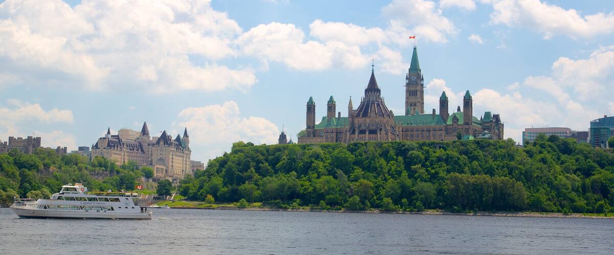 A river with a cruise ship, a large green-roofed building with towers, and a castle-like structure in the background.