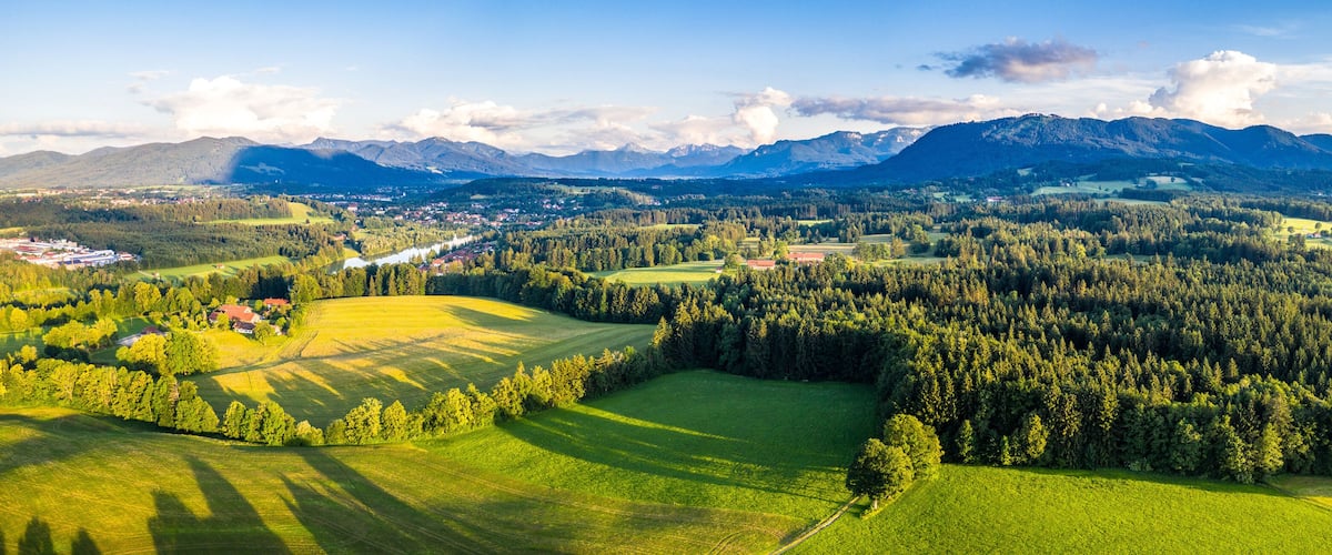 A mountainous landscape with a village, green fields, and dense forests.