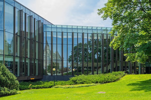 A modern glass building with a reflective facade, surrounded by a well-maintained grassy area and trees.