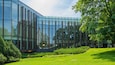 A modern glass building with a reflective facade, surrounded by a well-maintained grassy area and trees.