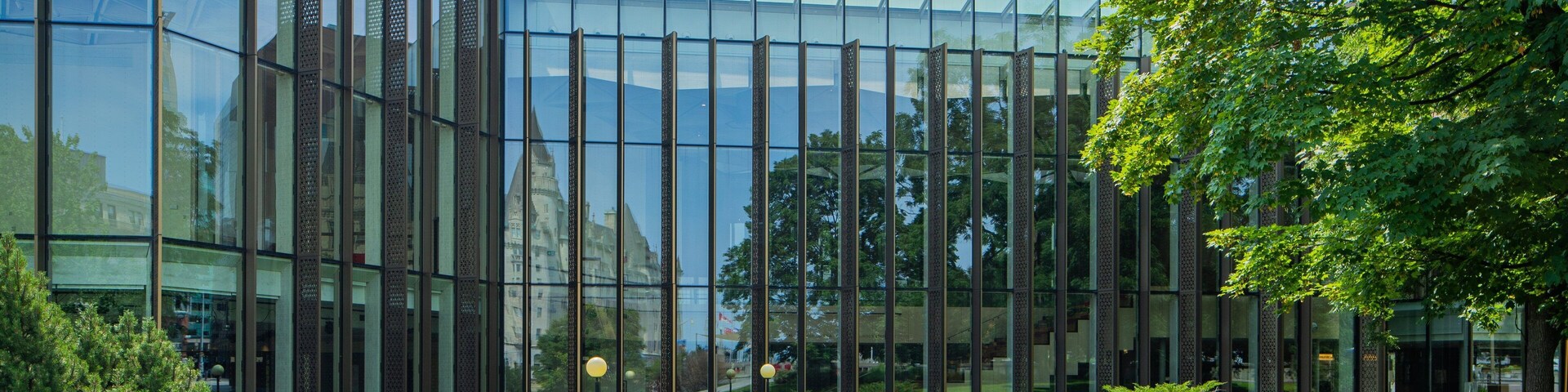 Un edificio moderno de vidrio con fachada reflectante, rodeado de un césped cuidado y árboles.